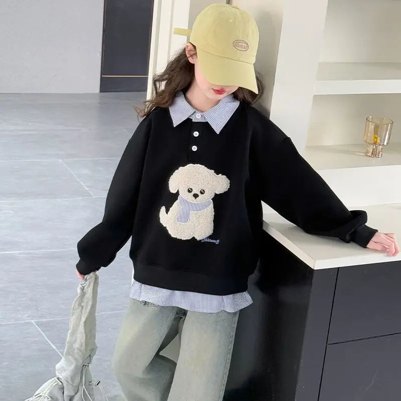Person wearing a black sweater with a dog design, light blue jeans, and a beige cap in an indoor setting.