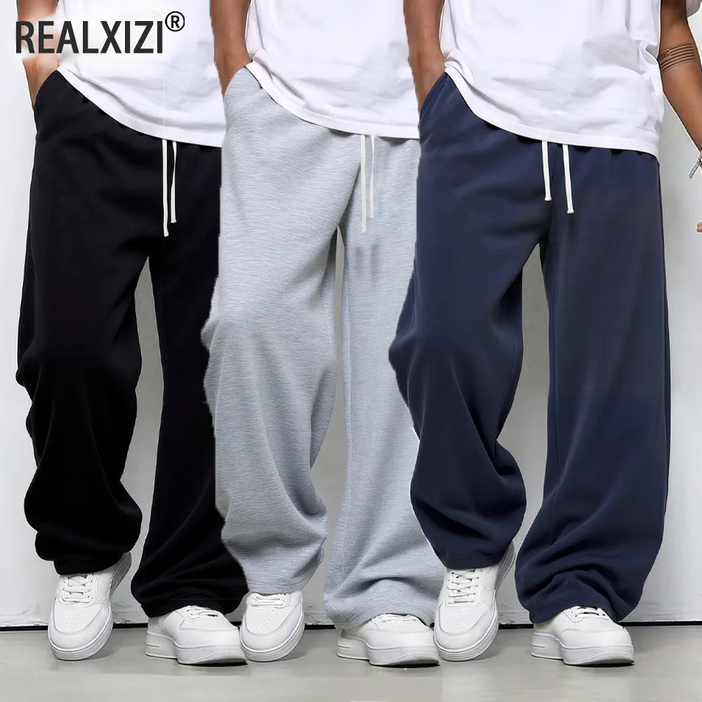 Three pairs of sweatpants in black, gray, and navy with white shoes on a plain background.