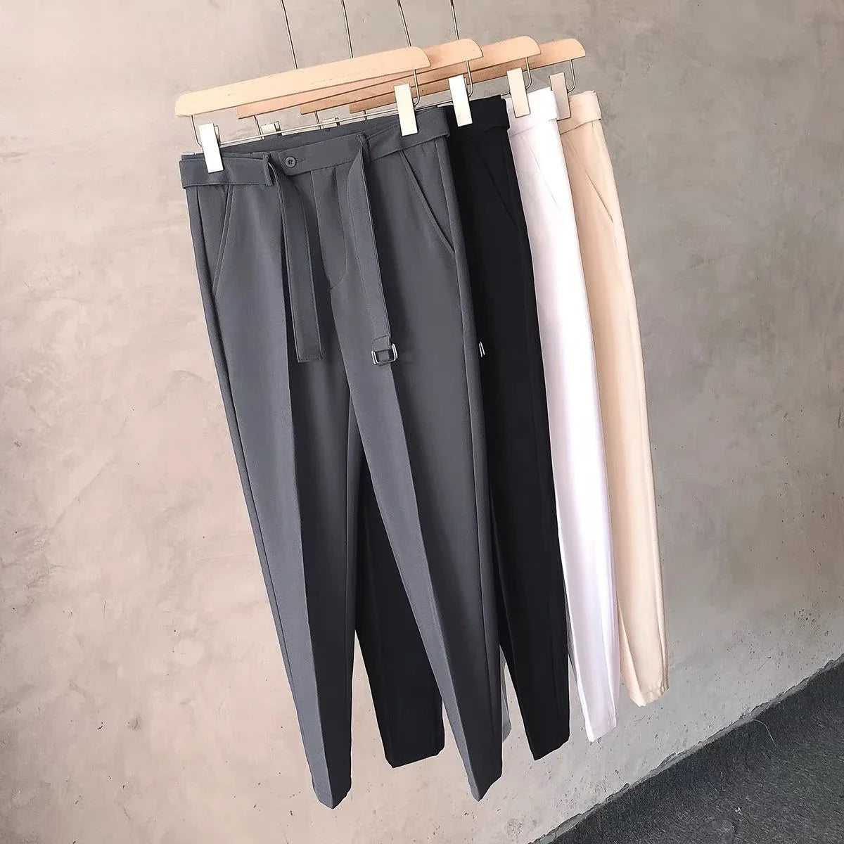 Three pairs of pants hanging on a rack against a neutral background