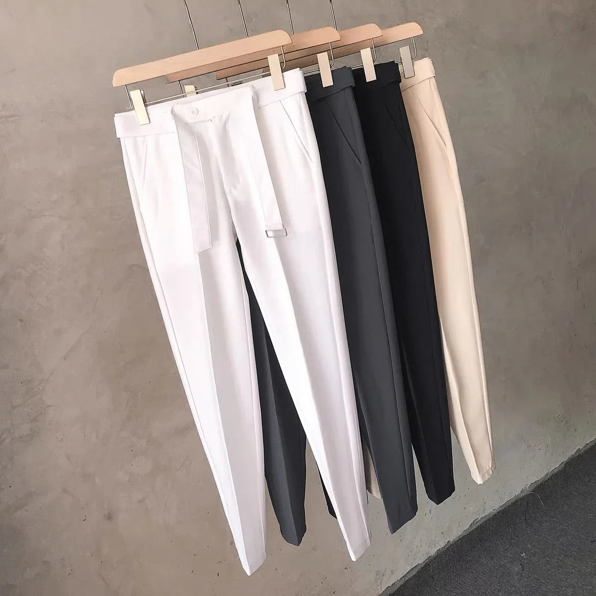 Three pairs of pants hanging on a rack against a neutral background