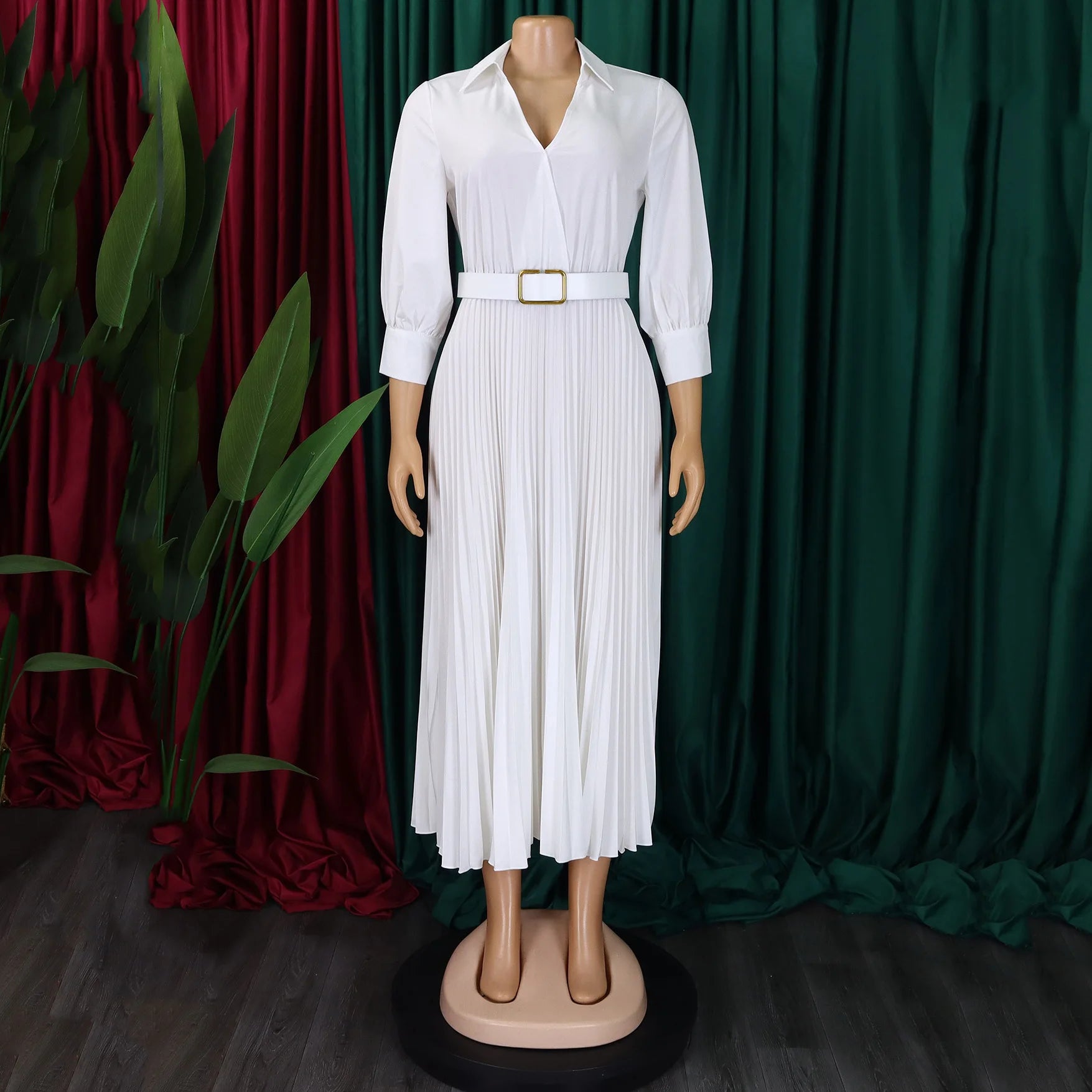 Mannequin wearing a white dress with a belt against a green and red curtain background