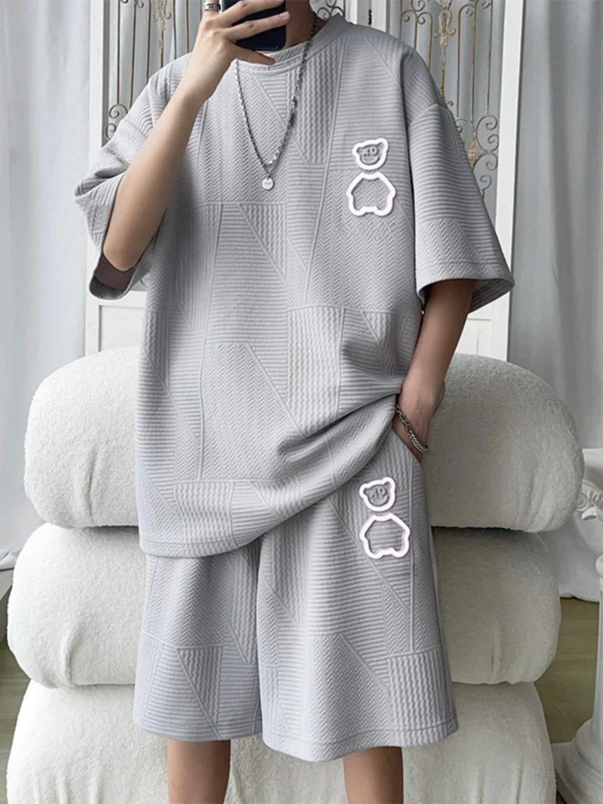 Person wearing a gray oversized sweater with bear face designs in a minimalistic room.