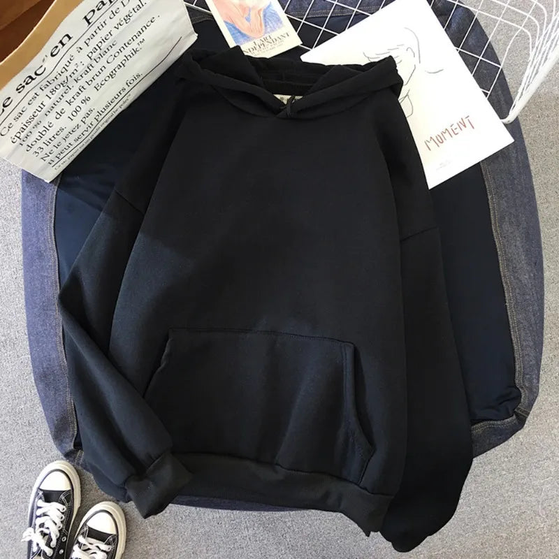 Black hoodie on a gray surface with a denim bag and sneakers in the background